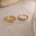 The Aquamarine Stacking Ring Set features two gold boho rings with ocean blue gemstones and clear accents, beautifully displayed on a light, textured surface.