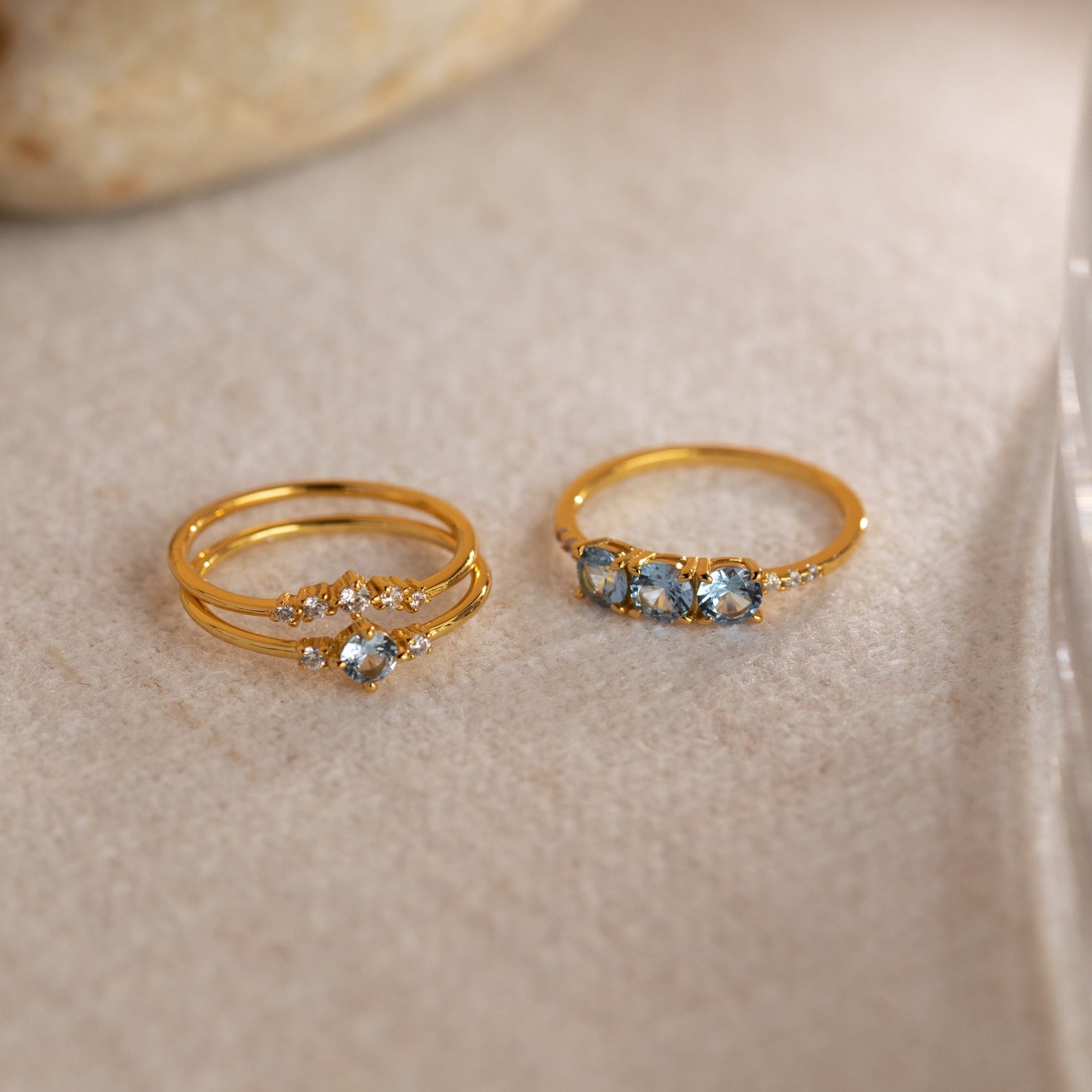 The Aquamarine Stacking Ring Set features two gold boho rings with ocean blue gemstones and clear accents, beautifully displayed on a light, textured surface.