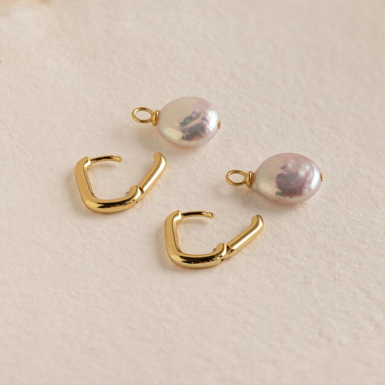 Two gold huggie hoops and two white pearl charms from the Bridget Pearl Hoops set, displayed on a light textured surface.