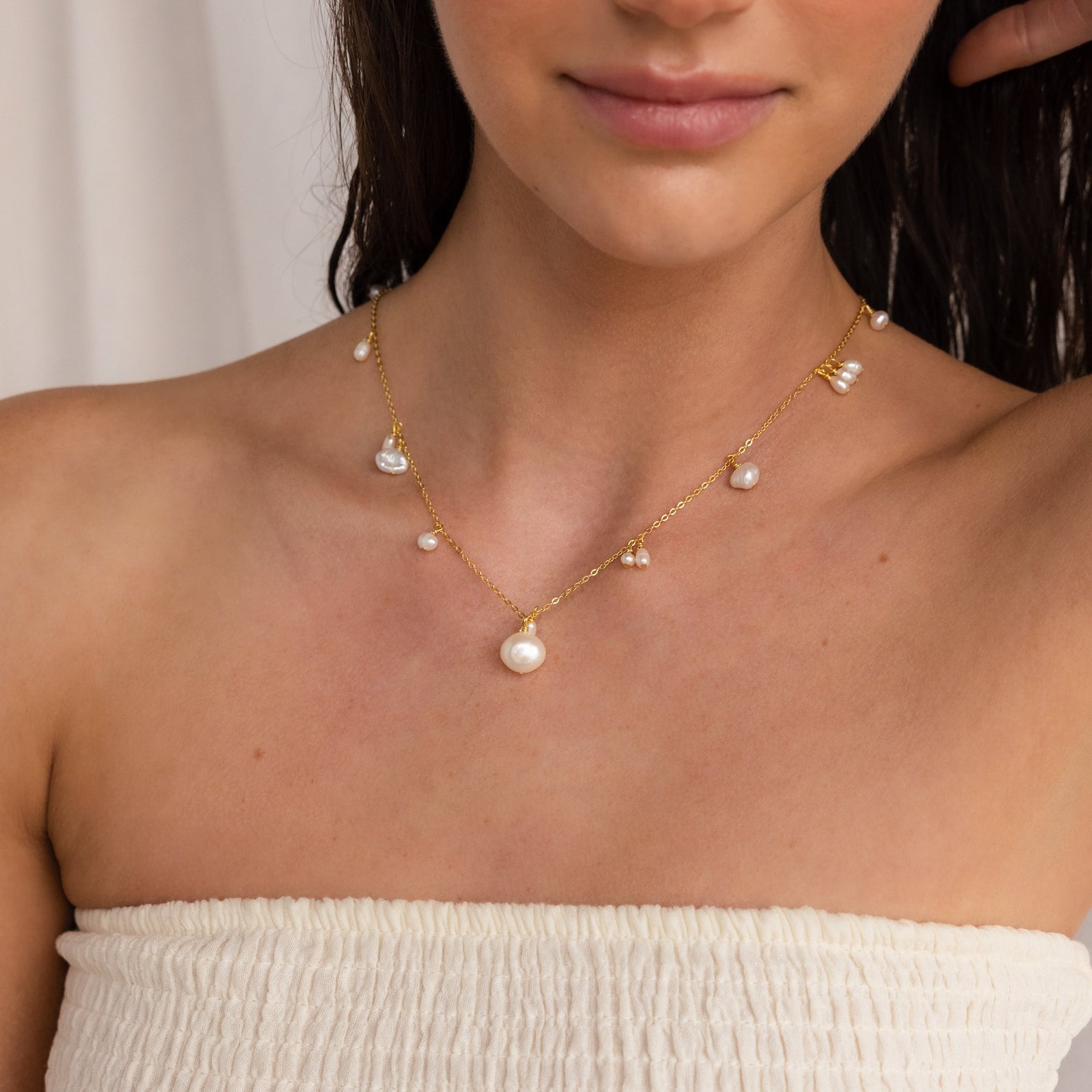 Woman wearing the Baroque Pearl Station Necklace featuring gold chain and small pearls, paired with a white textured strapless top.