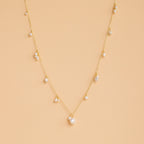 The Baroque Pearl Station Necklace in 18K Gold features a gold chain with spaced white pearls, displayed on a light beige background—an elegant choice for wedding jewelry.