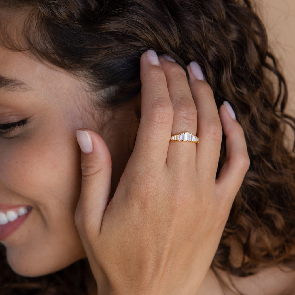Smiling woman with curly hair touches her face, showcasing a statement piece—the Art Deco Diamond Ring in Sterling Silver—highlighting its glamorous, vintage-inspired design.
