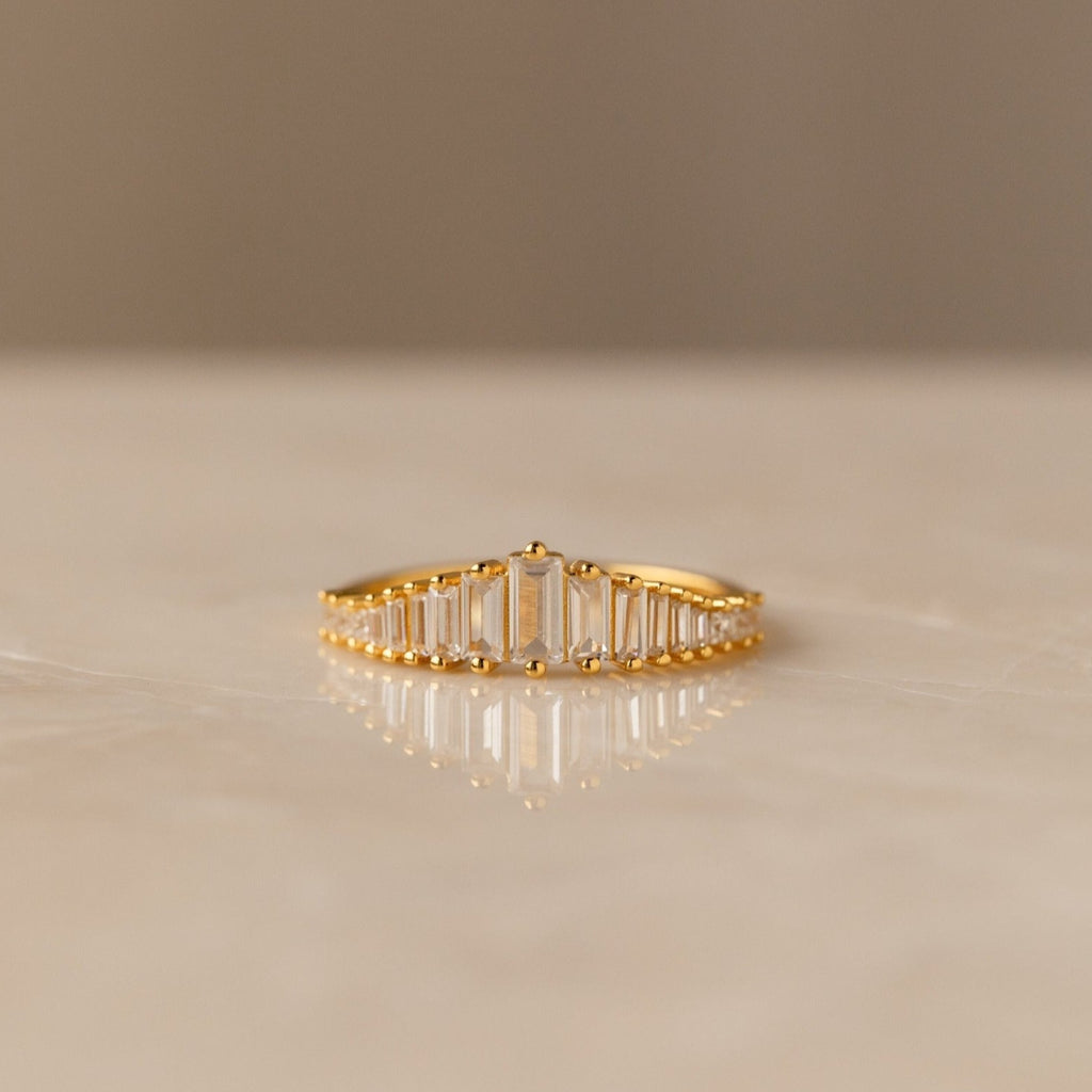 Art Deco Diamond Ring: A gold band adorned with a row of rectangular-cut clear stones, displayed elegantly on a smooth, light-colored surface—a bold statement piece.