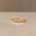 Art Deco Diamond Ring: A gold band adorned with a row of rectangular-cut clear stones, displayed elegantly on a smooth, light-colored surface—a bold statement piece.