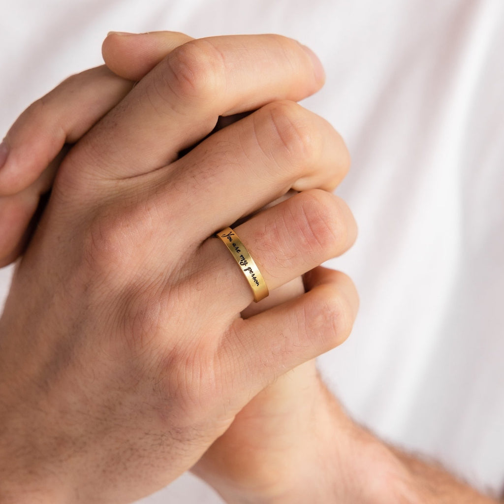A close-up of hands clasped together, wearing the Handwriting Band—a custom ring engraved with your own message—against a white shirt. A heartfelt Christmas gift idea.