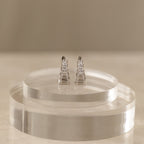 An Art Deco diamond earrings and ring set in sterling silver, elegantly displayed on clear, round acrylic stands against a neutral background.