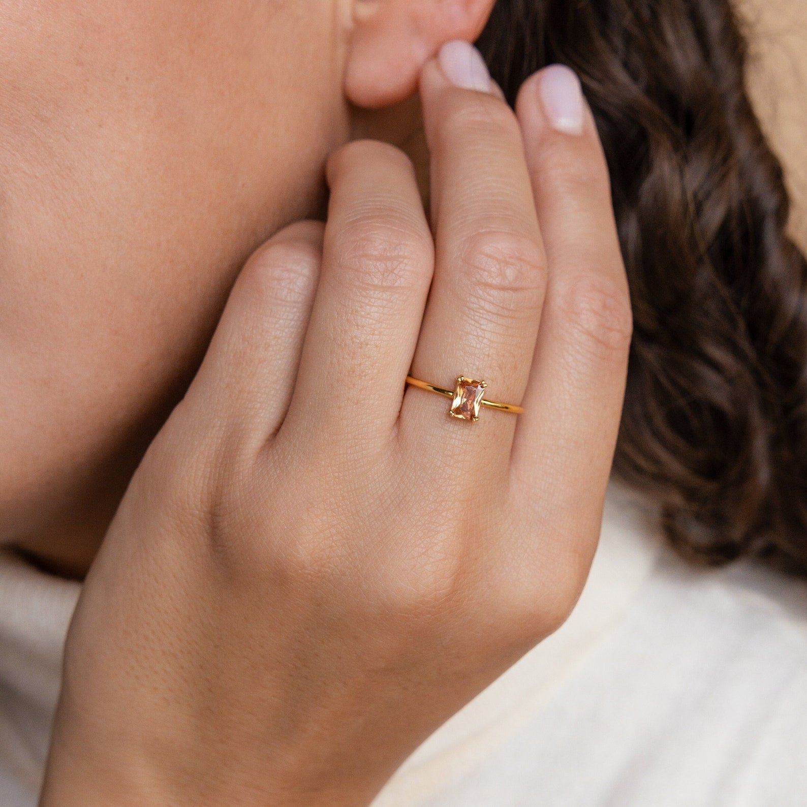 A hand wearing the Citrine Emerald Ring is held near the face, with curly brown hair visible in the background.