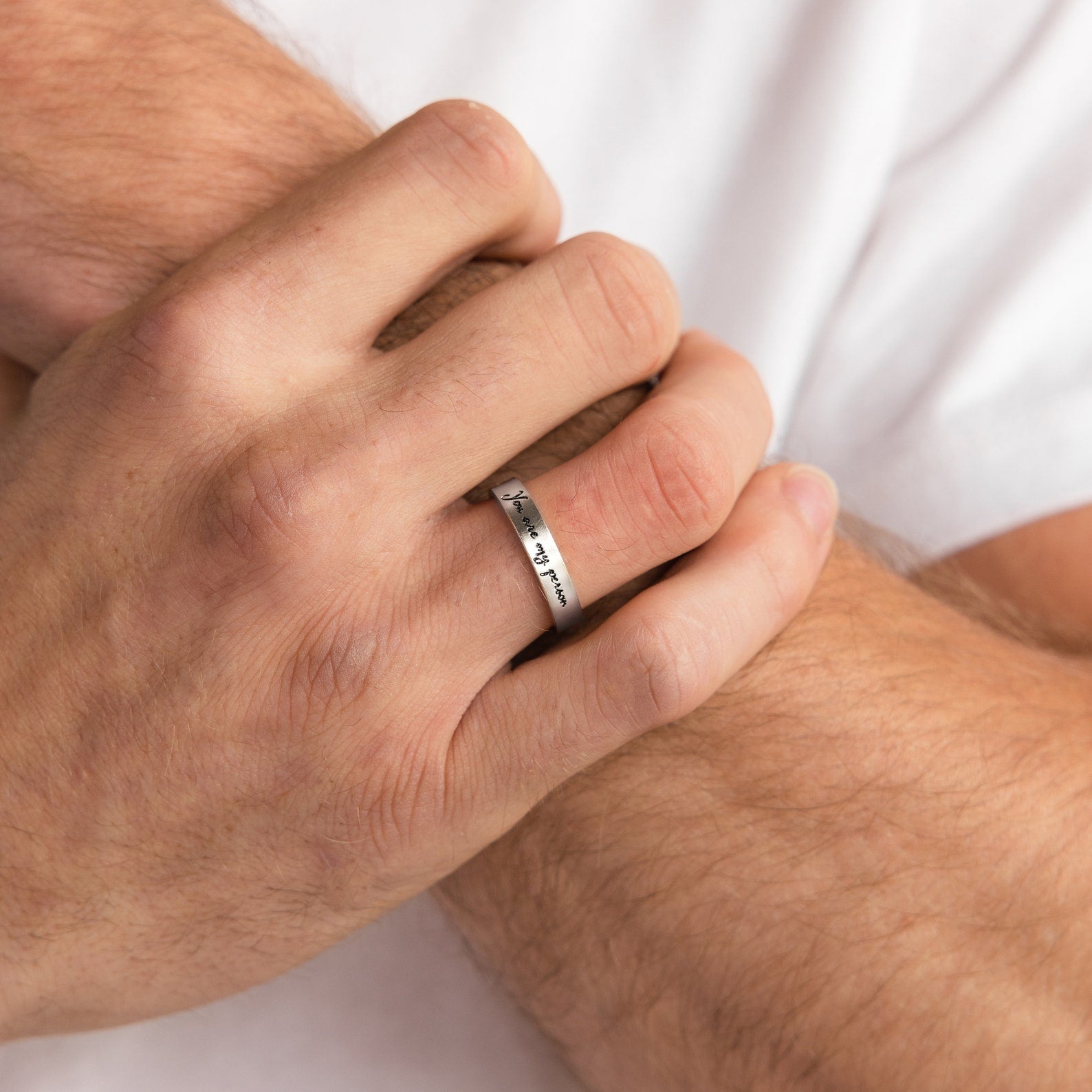 A hand wearing the Handwriting Band, engraved with a unique design, rests on a crossed forearm—this personalized ring is an ideal Christmas gift.