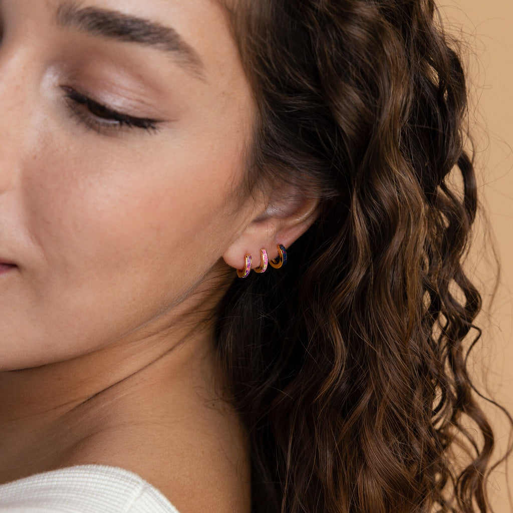 Close-up of a woman with long curly hair, wearing a white top and Magenta Opal Inlay Huggies.