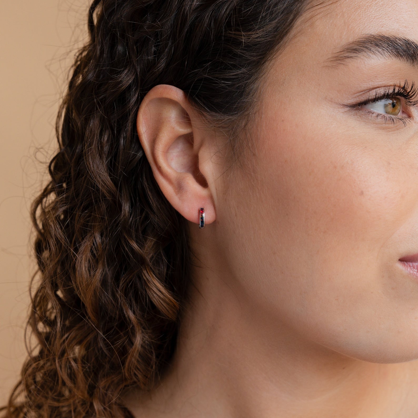 Close-up of a woman's ear wearing Black Opal Inlay Huggies against a neutral beige background.