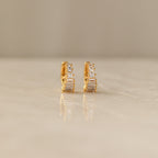 Close-up of a pair of gold Art Deco Huggie earrings on a marble surface, featuring a symmetrical arrangement of baguette and round-cut diamonds for a tiered, structured look.