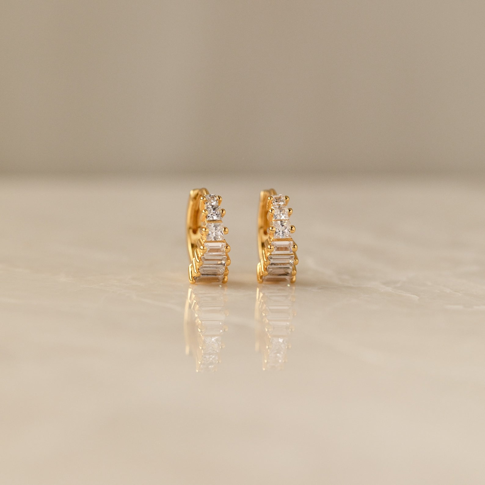 Close-up of a pair of gold Art Deco Huggie earrings on a marble surface, featuring a symmetrical arrangement of baguette and round-cut diamonds for a tiered, structured look.