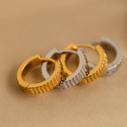 Two gold and two silver Ribbed Huggies with a ridged texture are daintily arranged on a beige surface.