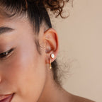 A close-up of a woman's ear adorned with the Oval Opal Studs, featuring a shimmering white opal stone in an elegant oval setting.