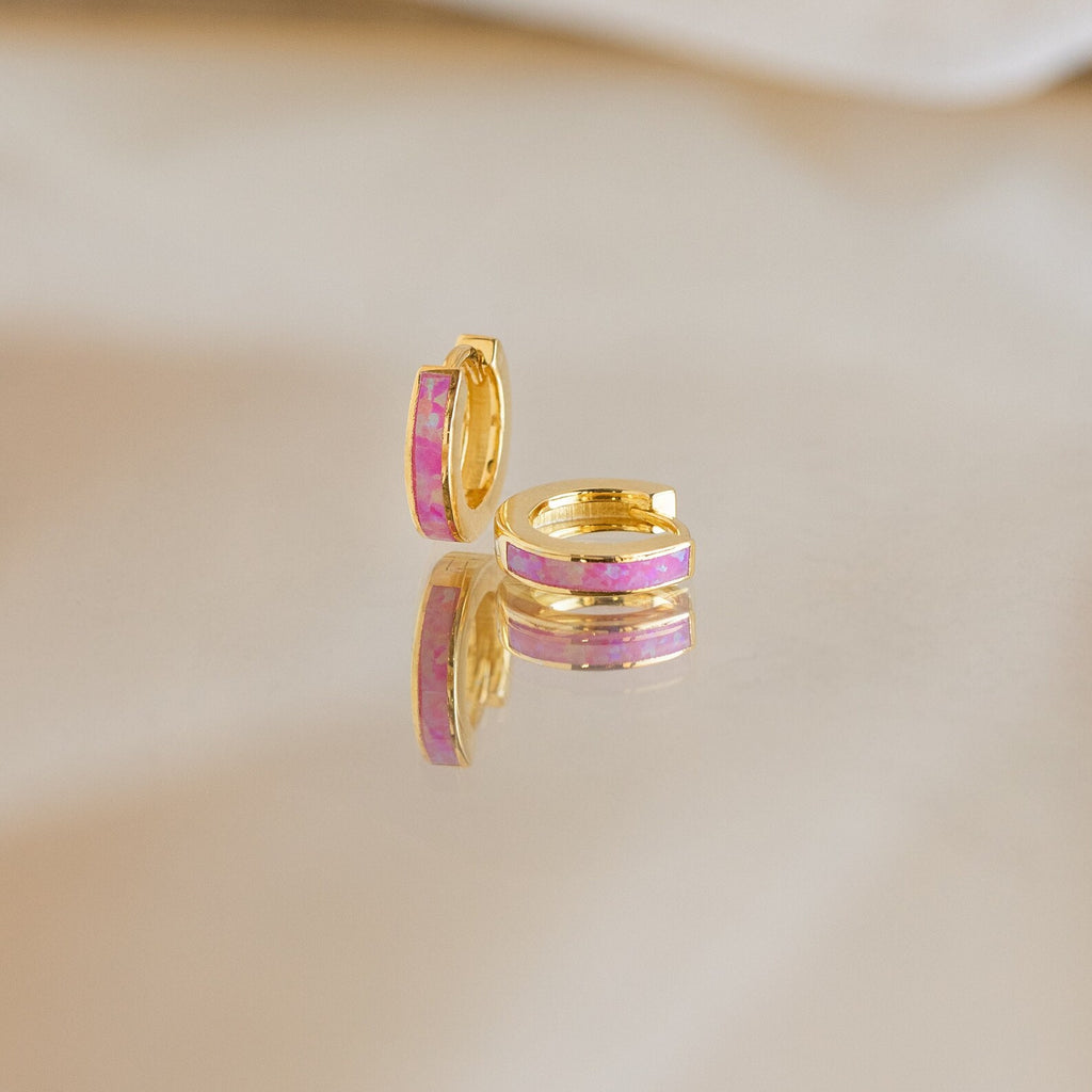Magenta Opal Inlay Huggies are showcased on a reflective surface with a soft background.