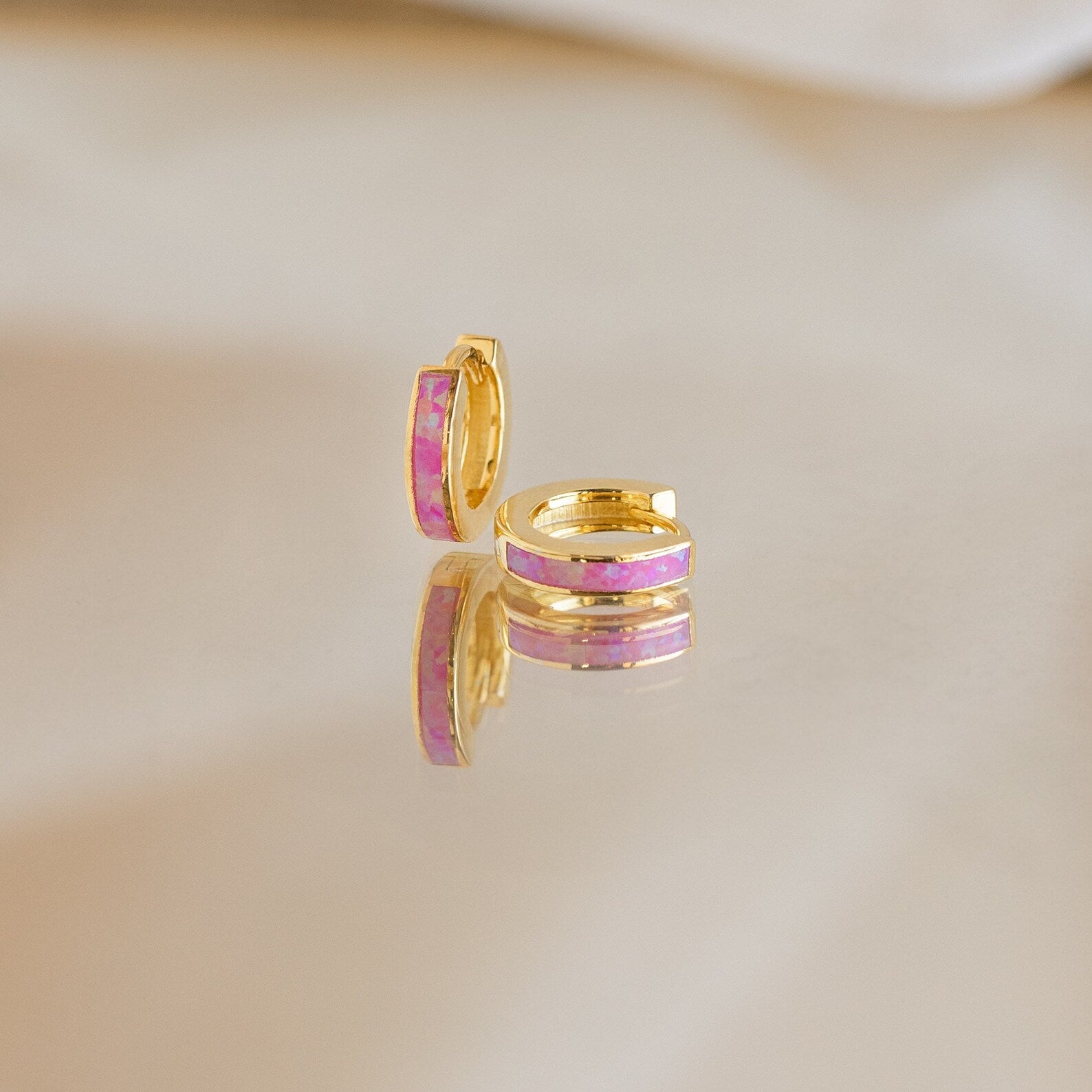 Magenta Opal Inlay Huggies are showcased on a reflective surface with a soft background.