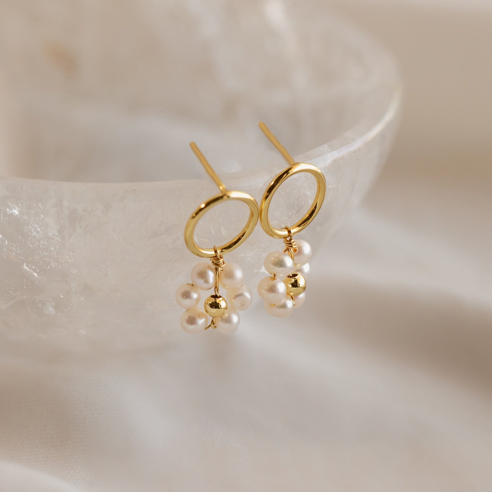 The Flower Pearl Drop Earrings feature clusters of small white pearls, capturing vintage charm and elegance, beautifully presented on a translucent textured surface.