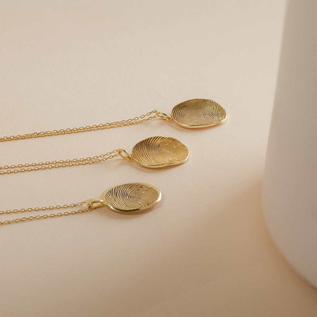 Three Custom Fingerprint Necklaces in Rose Gold with round engraved fingerprint pendants rest on a beige surface—each piece is a unique and sentimental gift.
