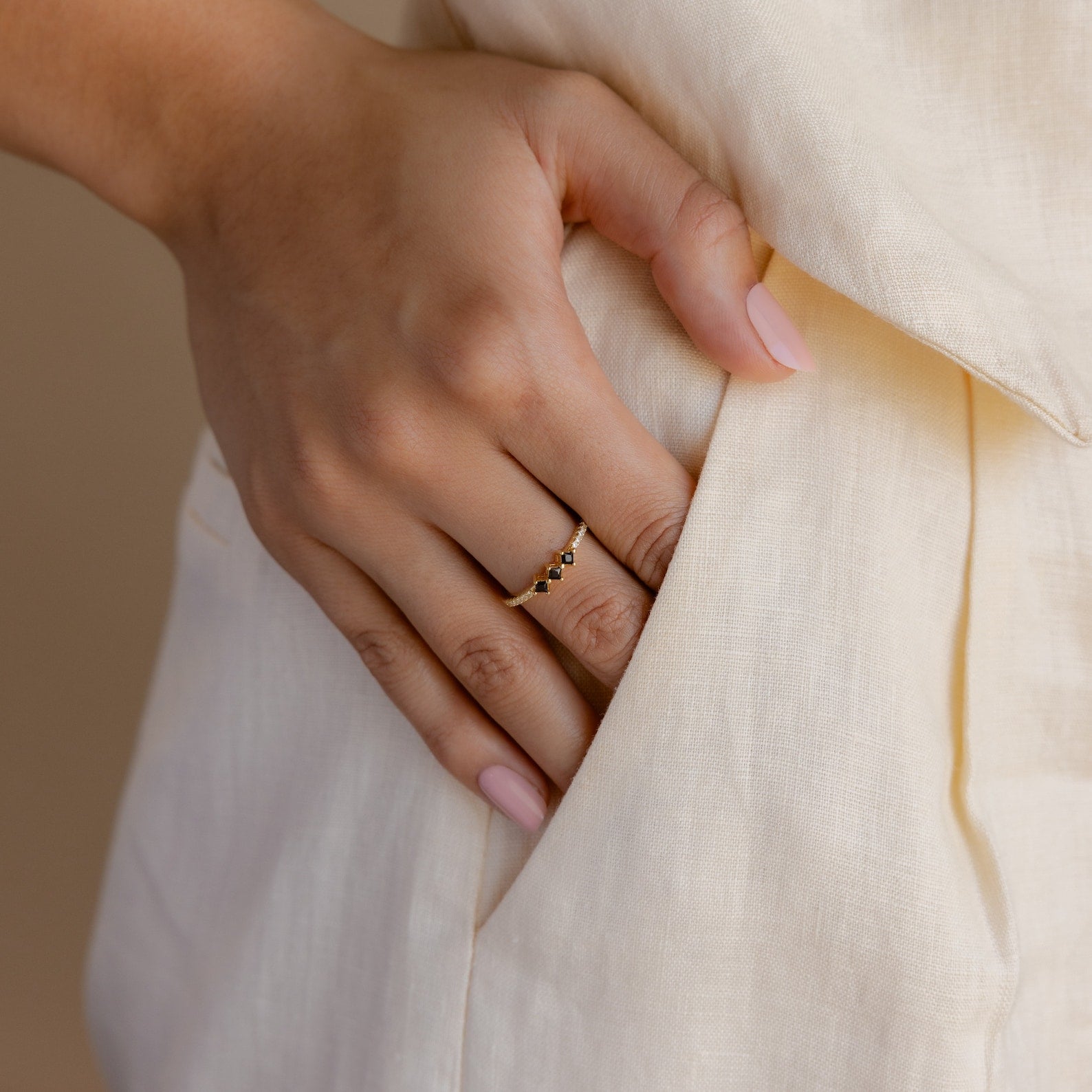 A hand adorned with the Helena Black Diamond Ring and pale pink nails rests on the pocket of a light-colored garment, creating an edgy yet professional vibe.