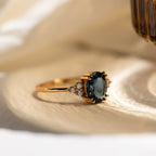 Close-up of the Elizabeth ring on a soft fabric surface, showcasing the oval-cut blue topaz and side stones.