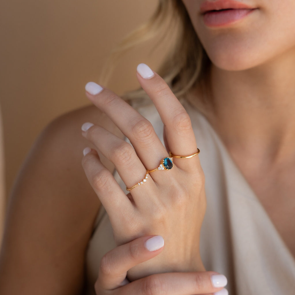 Woman wearing three gold rings, featuring the Elizabeth ring with a vivid blue gemstone at the center.