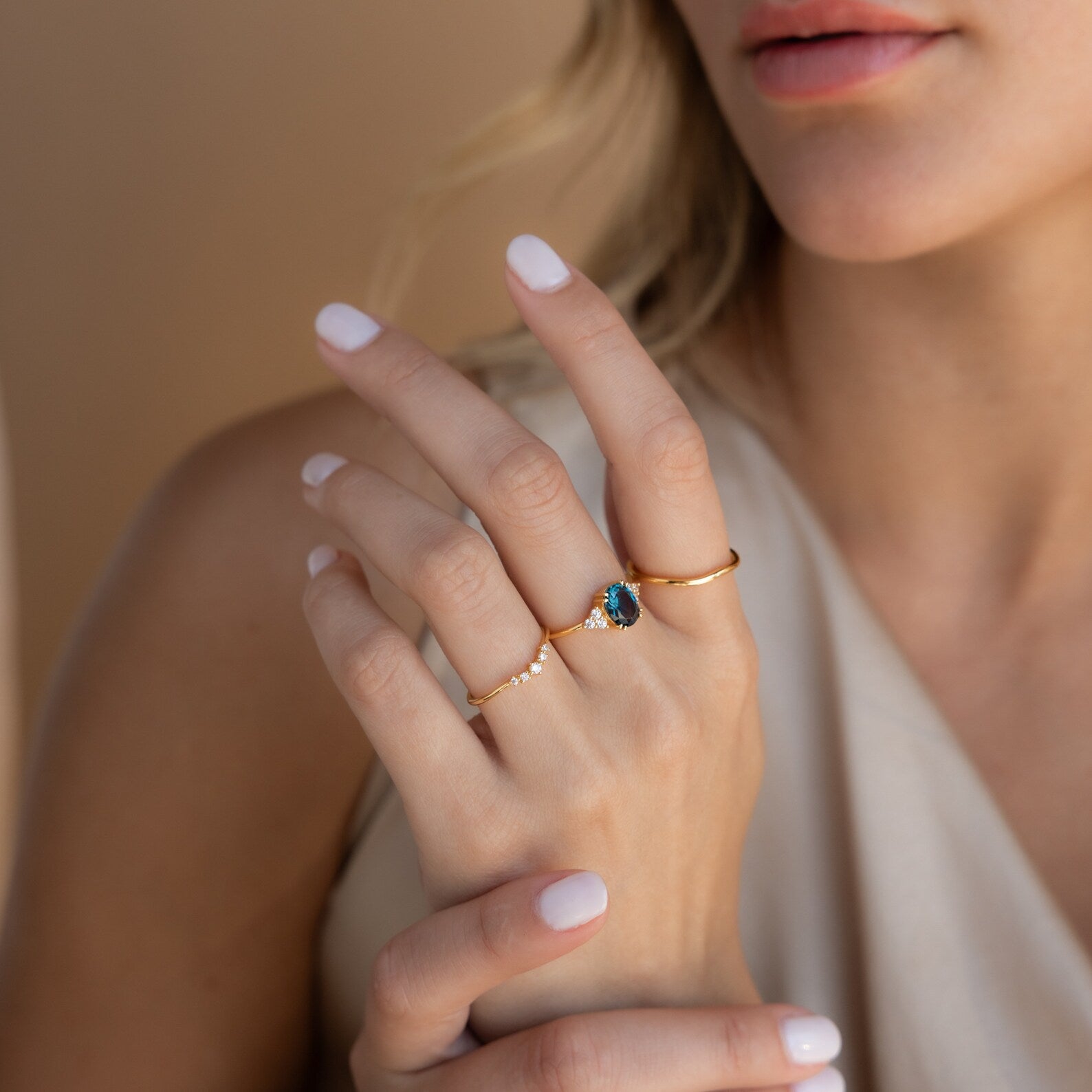 Woman wearing three gold rings, featuring the Elizabeth ring with a vivid blue gemstone at the center.