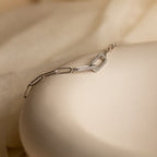 The Pave Link Chain Bracelet features delicate geometric links in silver, resting on a cream-colored surface—a minimalist and understated statement piece.