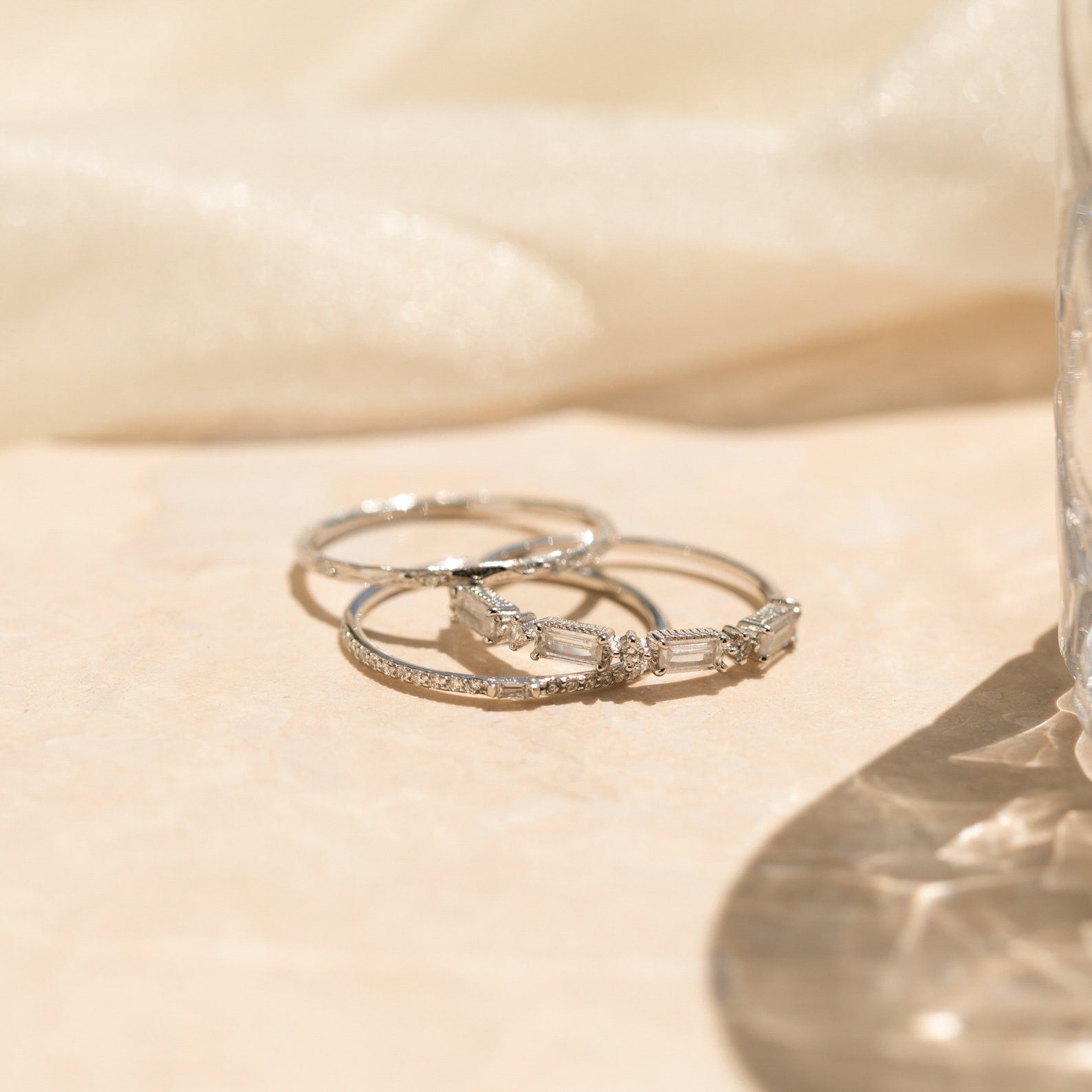 The Diamond Stacking Ring Set in Sterling Silver is shown stacked together on a light beige surface with soft sunlight and gentle shadows—a perfect Christmas gift.