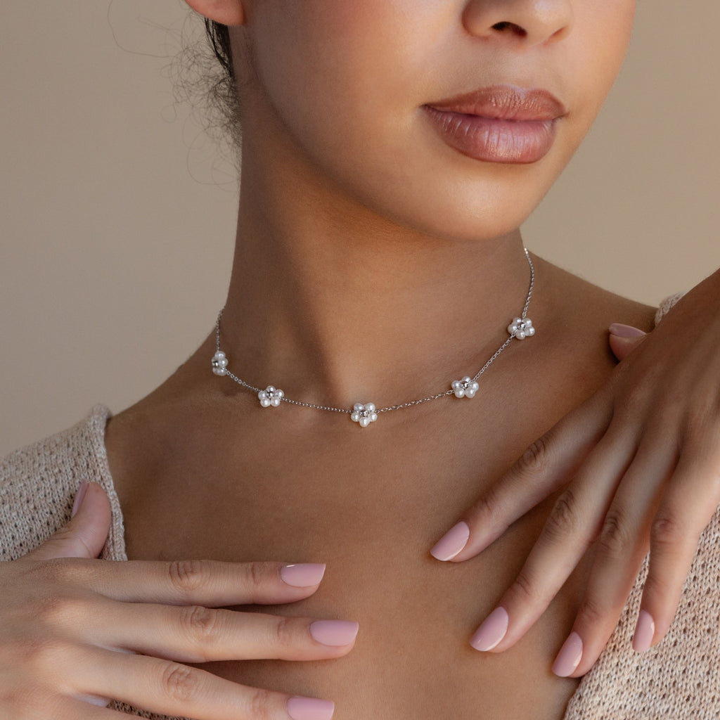 A woman wears the Flower Pearl Station Necklace—delicate silver with flower-shaped charms and pearls—making it an elegant Mother’s Day or bridesmaid gift.
