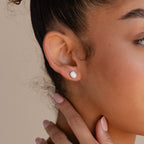 Close-up of a woman's ear wearing Oval Opal Studs, elegant earrings featuring a luminous white opal. Her hand touches her neck, nails painted light pink.