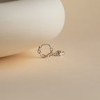 A single Link Huggies earring in silver rests on a smooth beige surface with a softly blurred background.