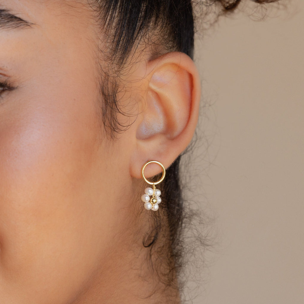 Close-up of a woman's ear wearing Flower Pearl Drop Earrings—gold hoops adorned with dangling white pearl-like beads for a vintage-inspired look.