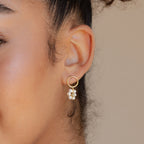 Close-up of a woman's ear wearing Flower Pearl Drop Earrings—gold hoops adorned with dangling white pearl-like beads for a vintage-inspired look.