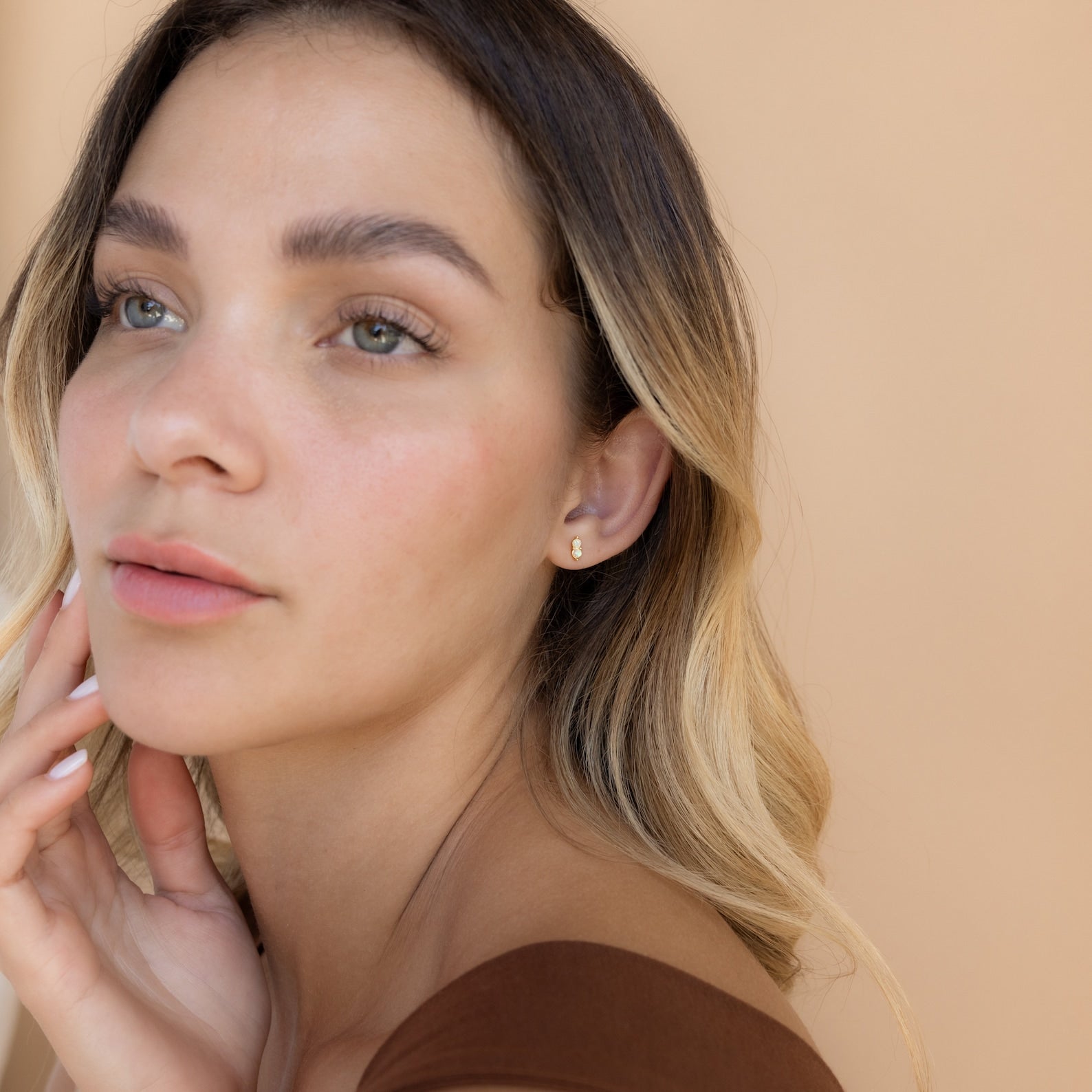 A woman with her hand on her face, elegantly showcasing the Duo Birthstone Studs—an ideal bridesmaids gift.