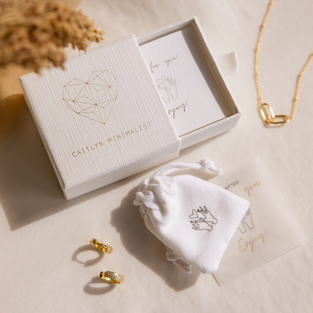 The Helena Black Diamond Ring is featured with gold earrings and a necklace, elegantly presented in a gift box and pouch on a cream surface—ideal for an edgy professional look.