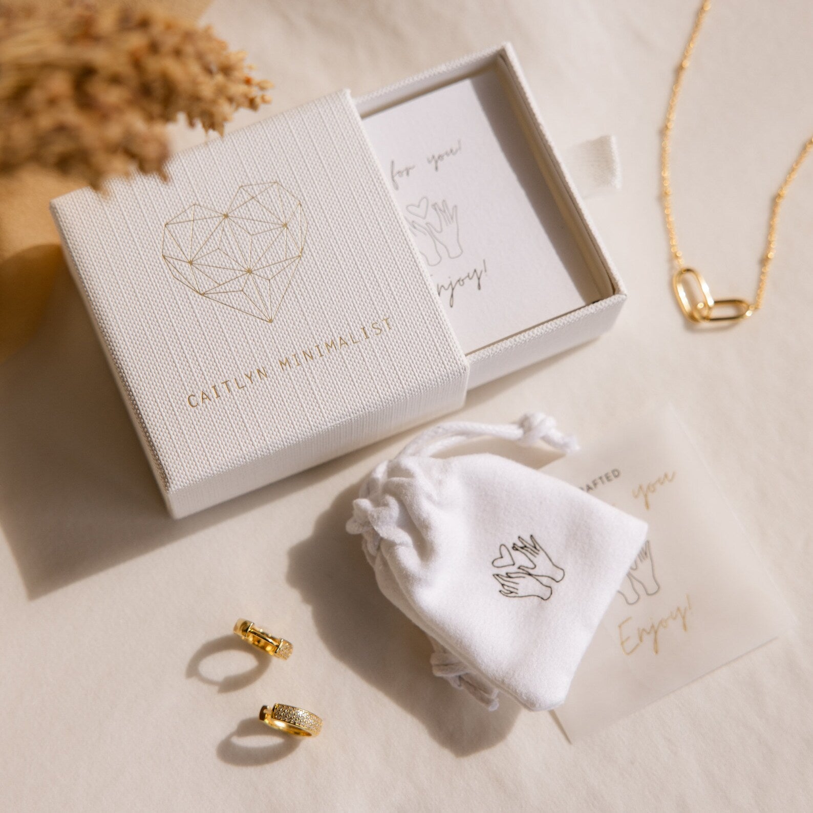The Helena Black Diamond Ring is featured with gold earrings and a necklace, elegantly presented in a gift box and pouch on a cream surface—ideal for an edgy professional look.