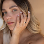 Woman gently touching her cheek while wearing the Elizabeth ring with blue topaz and gold band.