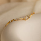 The Pave Link Chain Bracelet features a gold chain with a diamond-studded link, shown on a soft beige surface—a striking addition to any jewelry collection.