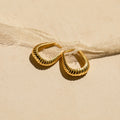 Bold Ribbed Hoops featuring subtle geometric designs rest on a light beige surface beside a sheer fabric ribbon.