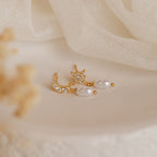 Moon & Star Pearl Earrings, featuring crystals, pearls, and a delicate pearl charm, shine beautifully against a soft beige fabric background.