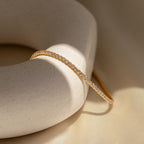 The Classic Diamond Tennis Bracelet in 18K Gold rests on a round, off-white stone, beautifully illuminated by soft natural lighting.