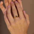 A hand with pink nails wears three stacked gold rings, including the Black Abyss Ring Set, which features delicate bands and a small black geometric stone.