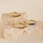The Morse Code Birthstone Ring and two other gold gemstone rings are displayed on two stacked beige stone slabs.