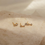 Triple Diamond Studs Set featuring small sparkling stones, presented on a textured beige stone surface in soft lighting.