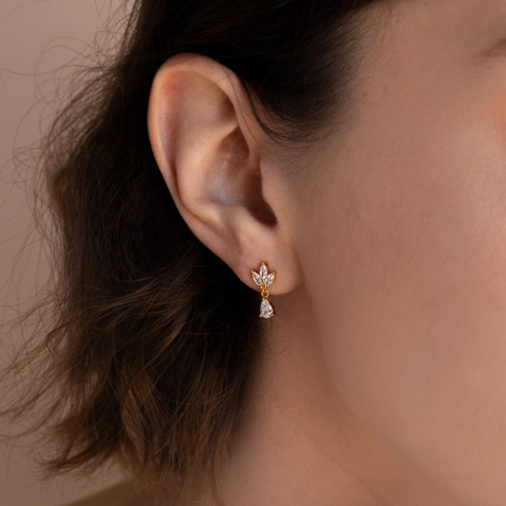 Close-up of a woman's ear wearing Marquise Diamond Drop Studs—gold earrings with a leaf design, marquise-cut diamonds, and a dangling teardrop gem.