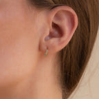 A close-up of a woman's ear adorned with an elegant earring stack, featuring the Garden Green Opal Huggies and green gemstone hoop earrings.