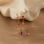 Mixed Pink Drop Earrings—romantic gold and silver earrings with pink gemstones—are displayed on a soft beige background with a shell prop.