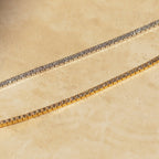 Close-up of two diamond tennis choker necklaces displayed on a sunlit stone surface—one with a white gold setting and the other with a yellow gold setting, both showcasing round-cut diamonds in a prong setting.