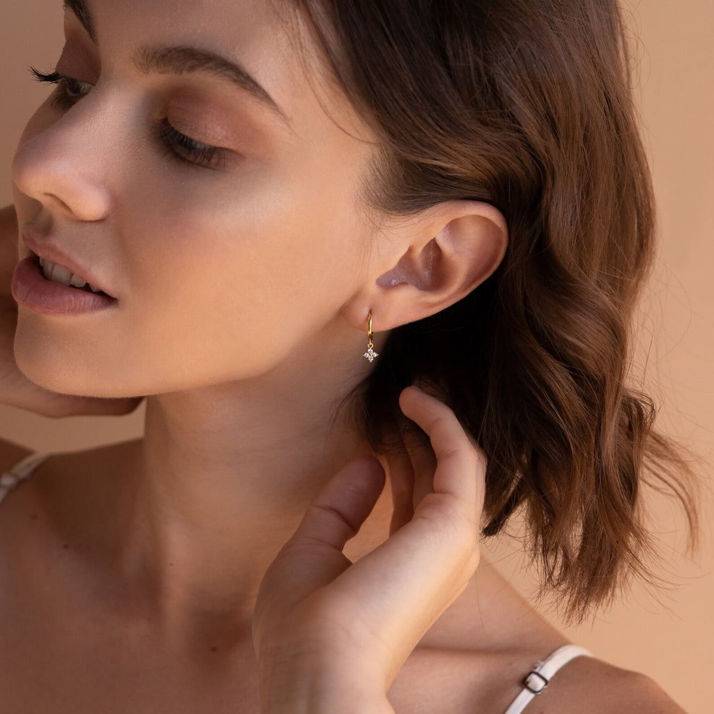 A woman poses with her head turned to the side, wearing a gold Diamond Flower Huggie in one ear
