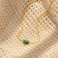 Minimalist gold necklace with a small horizontal jade bar pendant, displayed on a textured cream fabric background.
